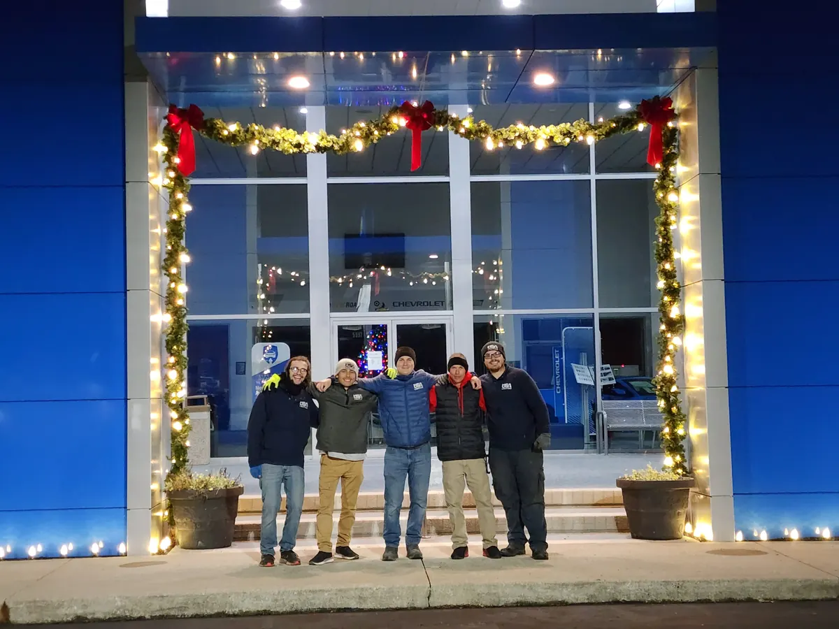 USA Lighting crew of five in branded apparel in front of a commercial holiday lighting install