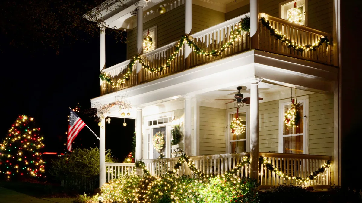 Lit Christmas garland and wreaths professionally installed on a two-story front porch with railing lighting