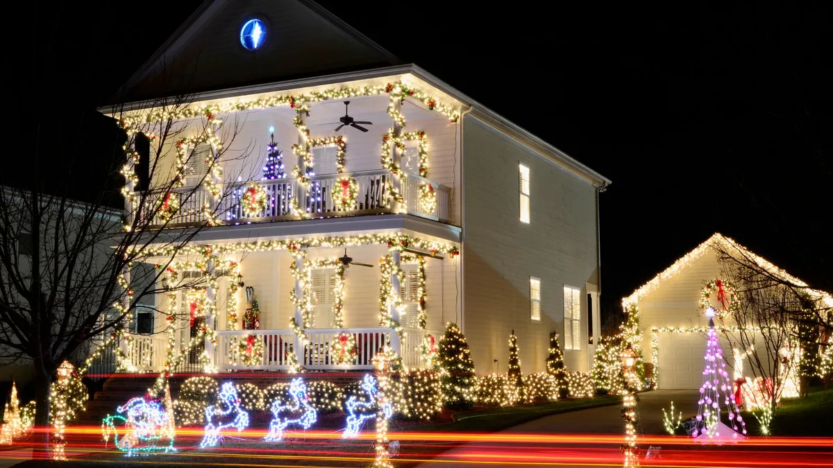 Custom holiday lighting display with lit garland-wrapped porches, wreaths, and multicolor yard decorations on a two-story home