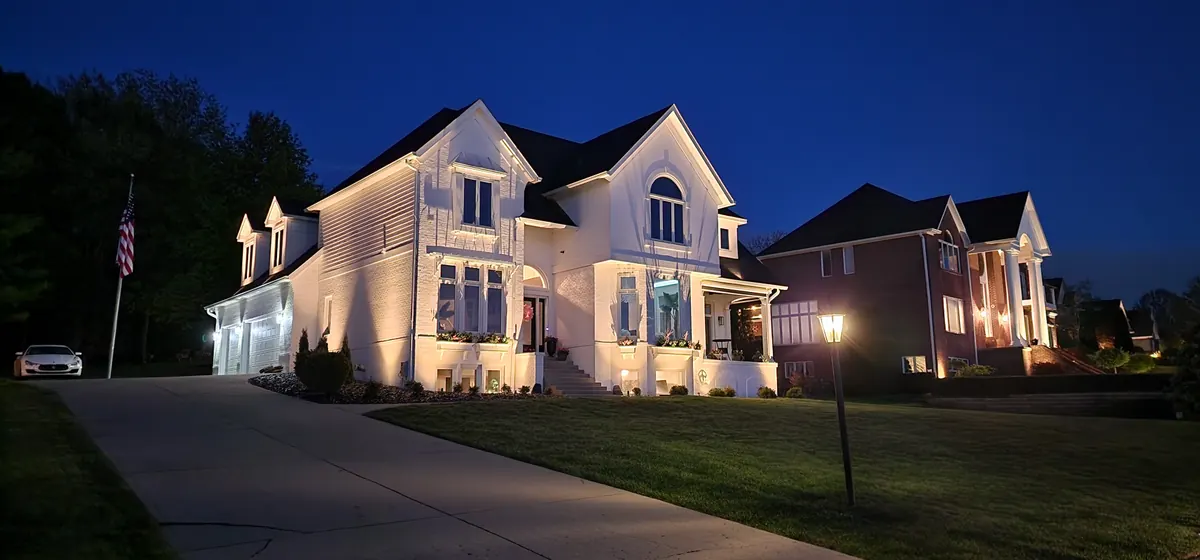 White two-story farmhouse with comprehensive warm-white facade uplighting