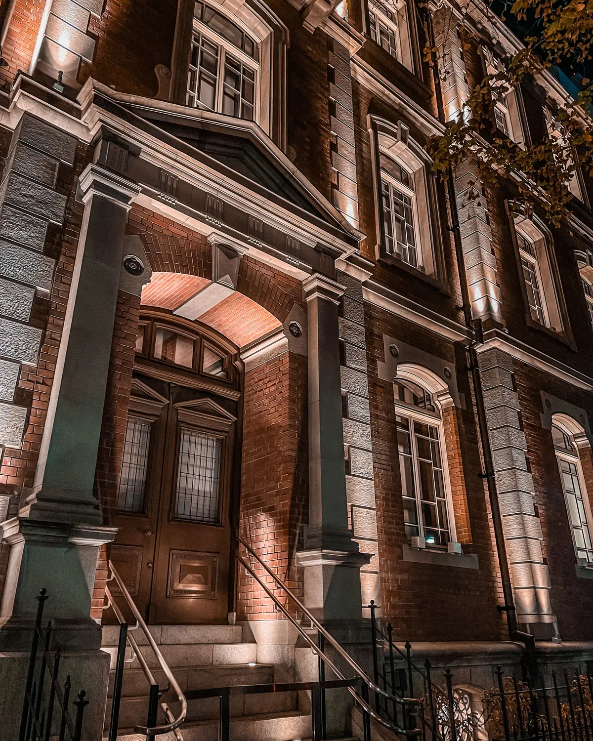 Historic brick and stone building facade at night with dramatic warm architectural uplighting on its grand entry
